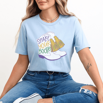 woman wearing light baby blue t-shirt that features a mardi gras design with Majorette dancer boots with the saying Shake Your Bootie